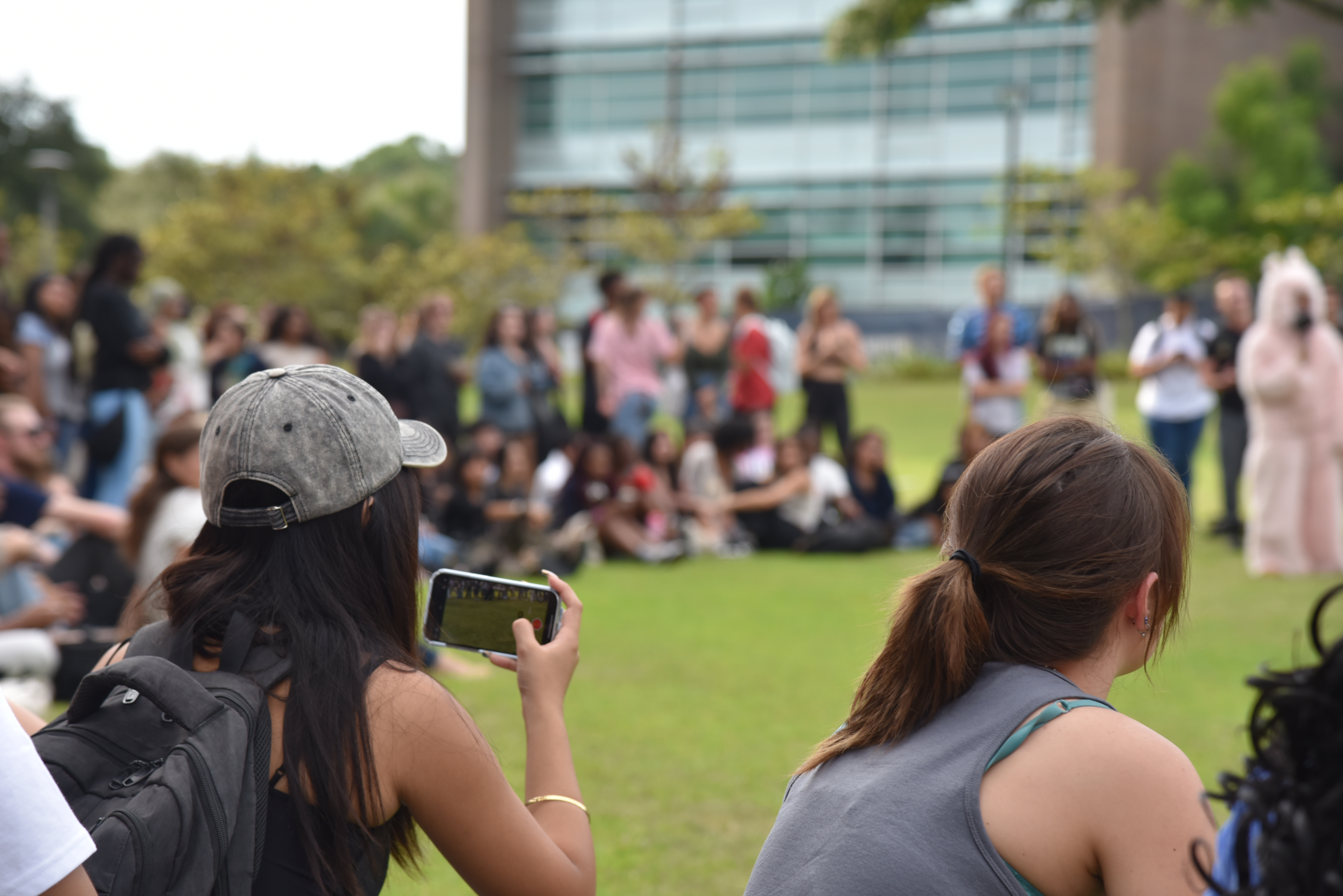 A student records the contest surrounded by other students while sitting near the green.